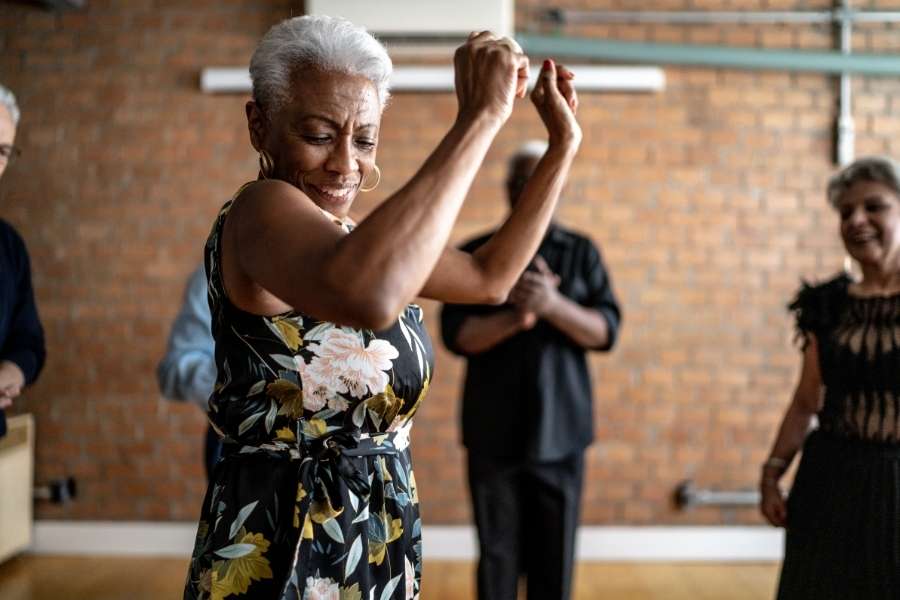 Une femme mature sourit en dansant joyeusement lors d'un cours de danse pour seniors.