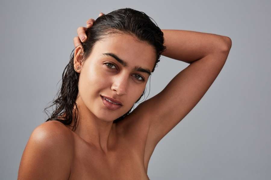 Une jeune femme souriante avec un make-up glowy et des cheveux mouillés.