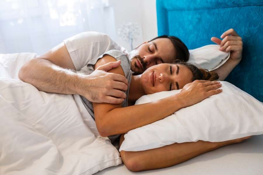 Un couple enlacé dort paisiblement dans un lit confortable.